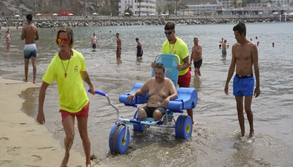 PRØVES: Badevaktene hjelper en innbygger ut og inn i vannet med den nye rullestolen i Puerto Rico.
