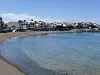 Sandstrand langs rolig bukt med lave hvite bygninger i bakgrunnen. Arguineguín på Gran Canaria.