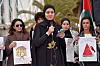 Wesam Hamada taler i mikrofon omgitt av demonstranter med plakater og palestinsk flagg.