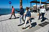 Flere personer går langs en solrik strandpromenade ved sjøen i Mogán.