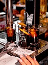 To glass med rød vermut på et metallbrett ved en bar, med menyark og en hånd nederst i bildet.