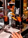 To glass med rød vermut på et metallbrett ved en bar, med menyark og en hånd nederst i bildet.